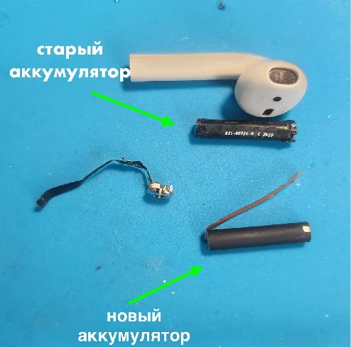 Разобранный наушник AirPods на синем коврике, рядом старый и новый цилиндрические аккумуляторы с подписями стрелками и плата с проводом