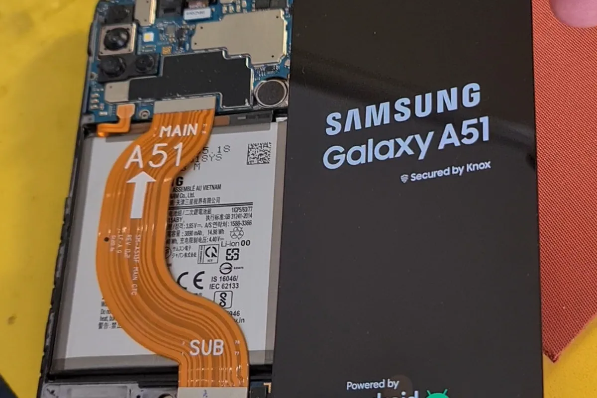 Разобранный Samsung Galaxy A51 с видимой платой и аккумулятором лежит рядом с фирменной коробкой аппарата