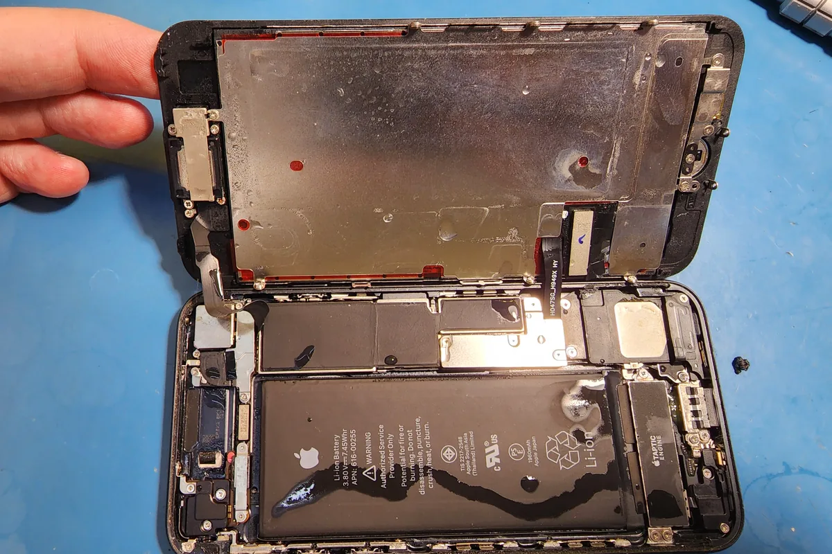 Разобранный iPhone на столе мастера: дисплей поднят, видны аккумулятор, шлейфы и внутренние крепления корпуса