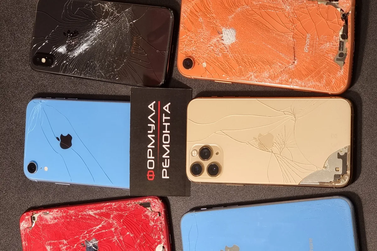 Несколько iPhone с разбитыми экранами и корпусами лежат на столе, на одном аппарате наклейка «Формула Ремонта»