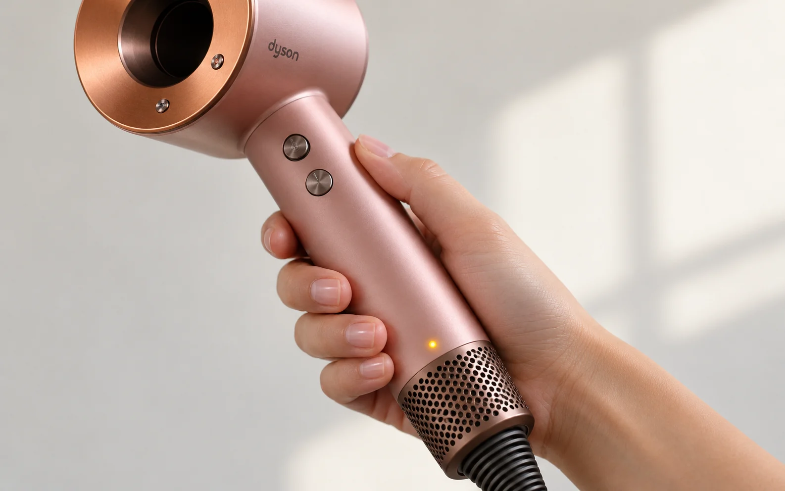 Рукоятка розового фена Dyson в руке, на корпусе горит жёлтый огонёк индикатора фильтра.