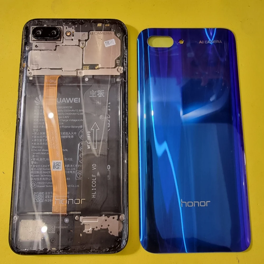 Разобранный Honor 10 на жёлтом столе: под прозрачной плёнкой виден аккумулятор, поверх него тянется оранжевый шлейф, рядом лежит синяя задняя крышка с надписью honor.
