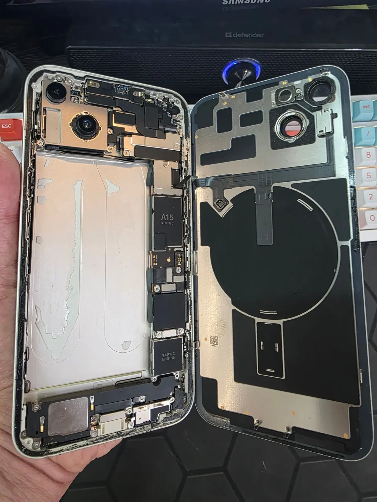 Открытый iPhone 14 со снятой задней крышкой и вынутым аккумулятором лежит на ладони, видна внутренняя рамка корпуса и плата