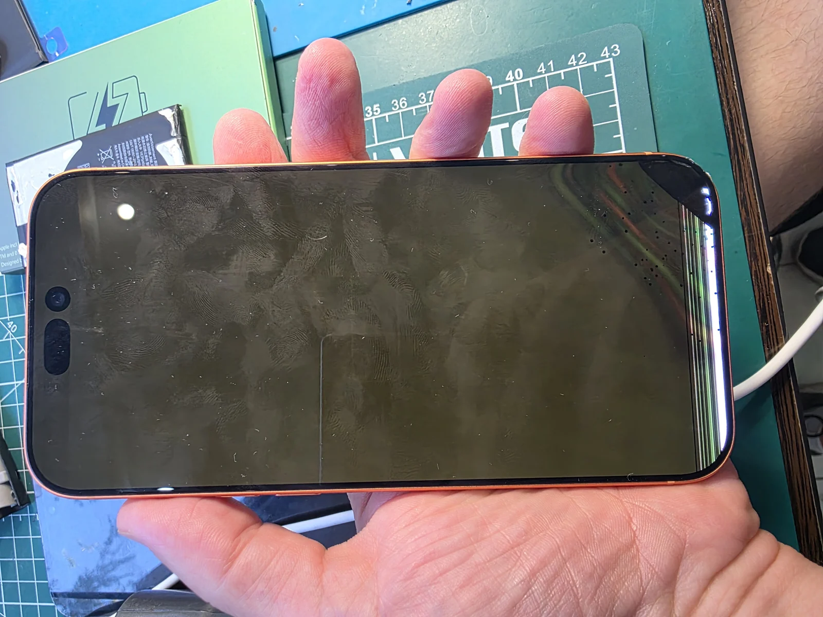 iPhone 17 Pro Max цвета Cosmic Orange в руке мастера: дисплей не показывает изображение, по краю экрана видна полоса из вертикальных цветных линий