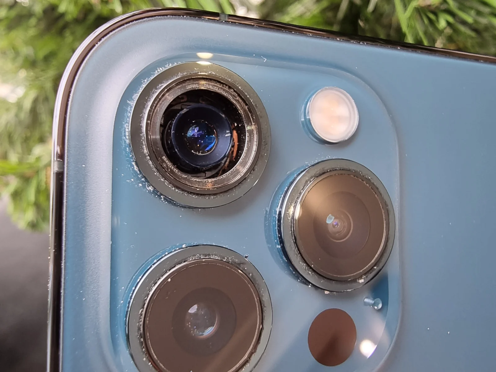 Блок из трёх камер iPhone 12 Pro крупным планом: у верхнего объектива нет защитного стекла, вокруг ободков белая крошка.