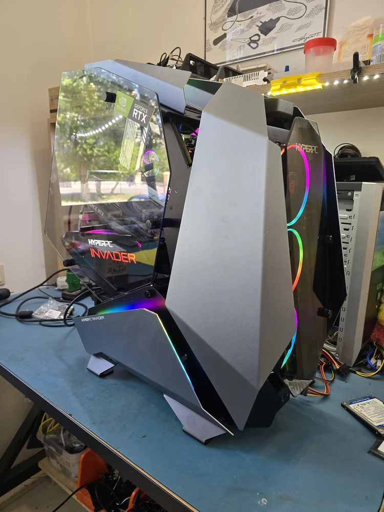 Собранный системный блок в корпусе с разноцветной RGB-подсветкой стоит на синем рабочем столе мастерской, рядом провода и инструменты.