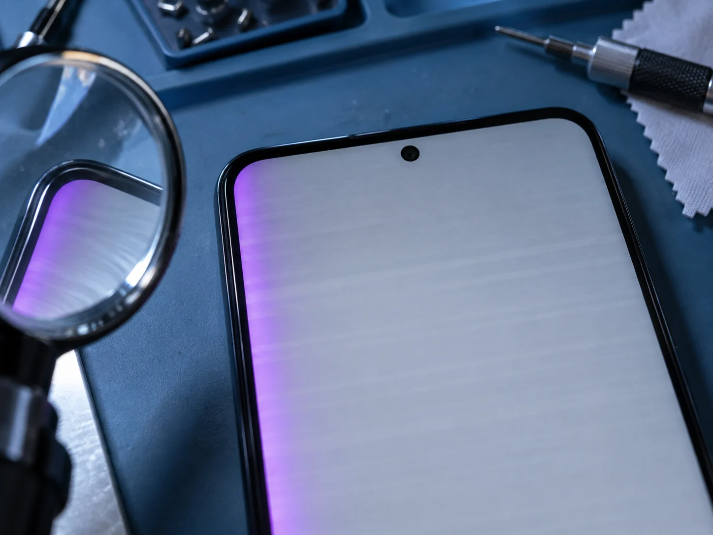 Верх экрана Samsung крупным планом: на сером фоне бледные полосы и фиолетовый отлив по краю, рядом лупа мастера