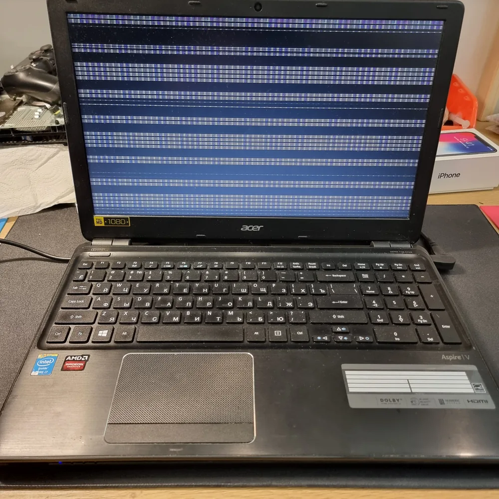 Раскрытый ноутбук Acer Aspire V на столе мастерской: экран включён и вместо изображения показывает широкие горизонтальные полосы синего и белого цвета по всей высоте