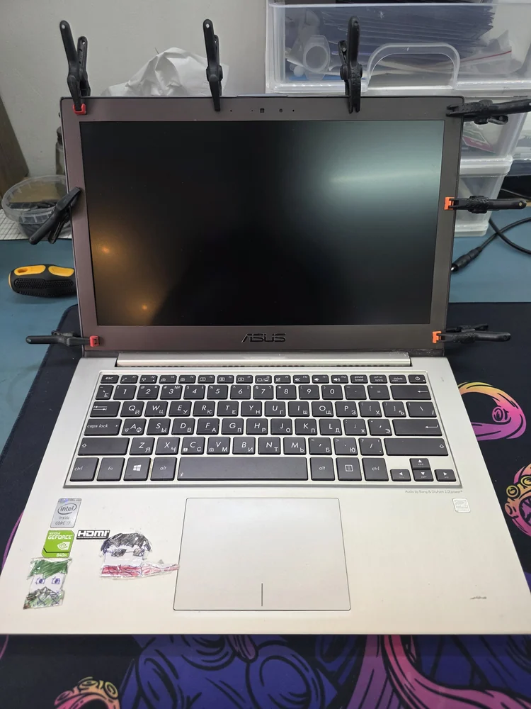 Ноутбук Asus на рабочем коврике мастерской: крышка с матрицей стянута по периметру десятью струбцинами после проклейки, экран выключен, рядом отвёртка