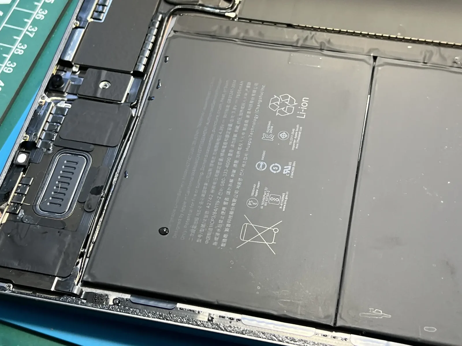 Внутренности залитого iPad со снятым дисплеем, на батарее и плате видны капли жидкости
