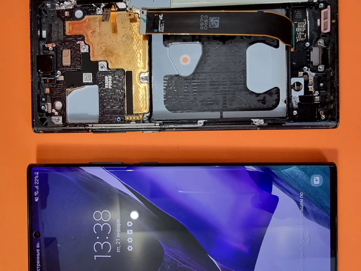 Два Samsung Galaxy Note 20 Ultra на оранжевом фоне: один разобран до материнской платы со шлейфами и модулями, второй лежит рядом целым