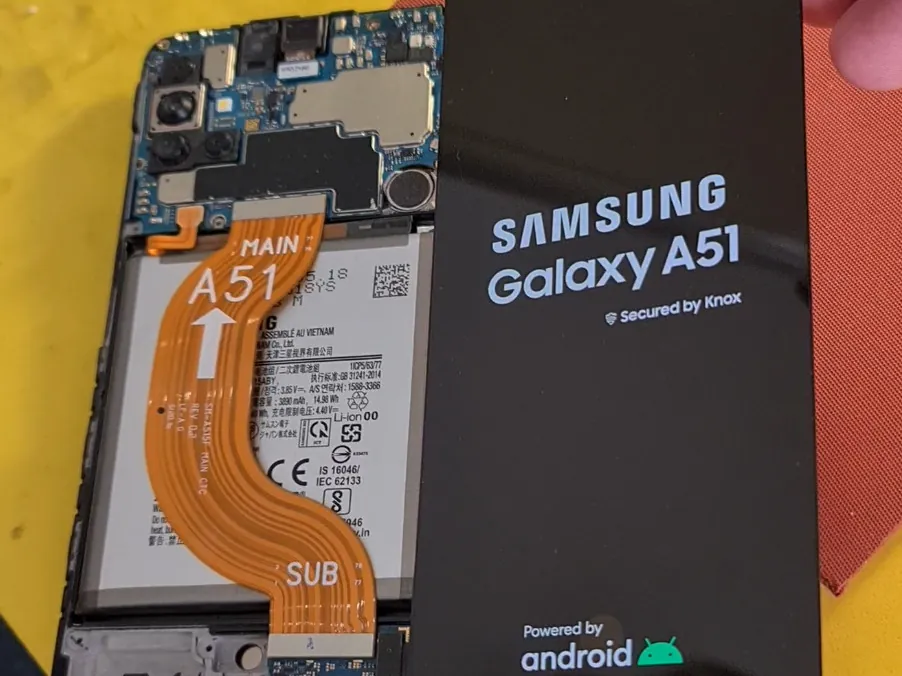 Разобранный Samsung Galaxy A51 на рабочем столе мастерской: видны материнская плата, аккумулятор и шлейфы, рядом лежит снятый дисплей