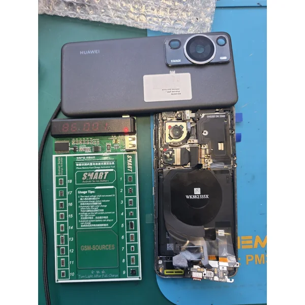 Разобранный Huawei P60 Pro на мате мастера рядом с активатором аккумуляторов: на дисплее платы горят цифры напряжения